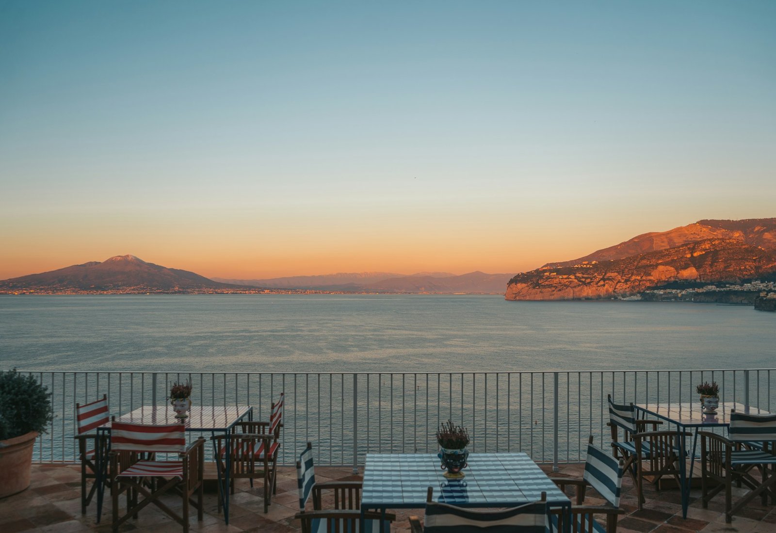 Terrazza di un ristorante mediterraneo al tramonto con vista mare e tavoli apparecchiati.